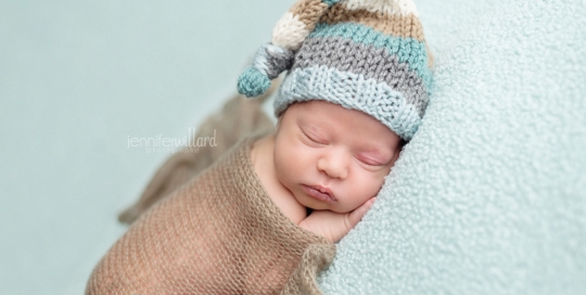 newborn baby boy on blue blanket with stripped hat