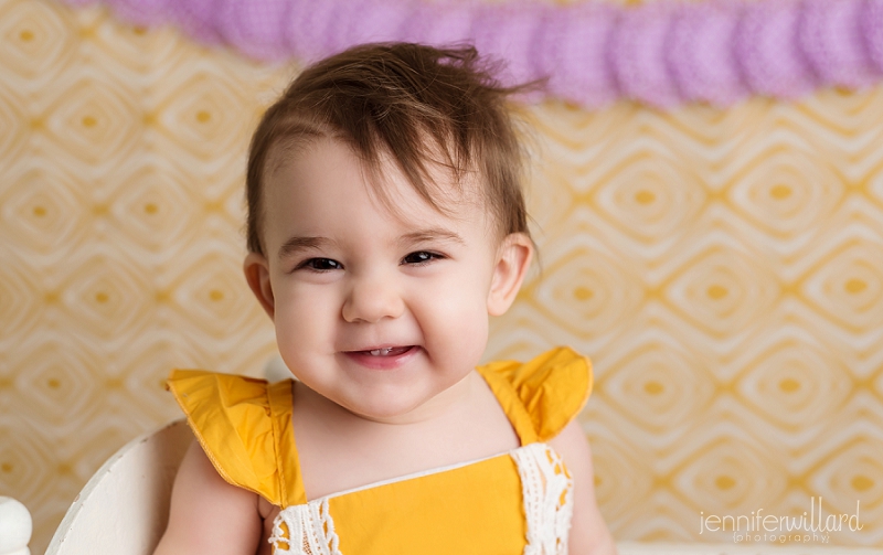 baby-girl-smiling-yellow-romper-spring-backdrop-purple-banner-kingston-portrait-studio