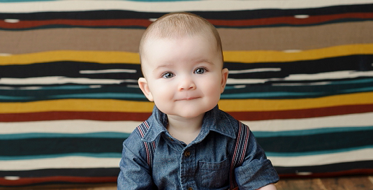 6 month old baby boy in blue shirt with suspenders on fall coloured stripe backdrop in Kingston Photography Studio