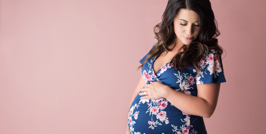 Maternity Portrait of Pregnant woman in flower dress on pink backdrop in Kingston Ontario