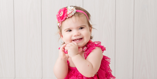 baby girl in pink romper on white backdrop with gold stars