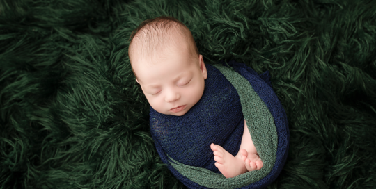 baby boy in blue and green wrap on green flokati rug in kingston ontario newborn studio