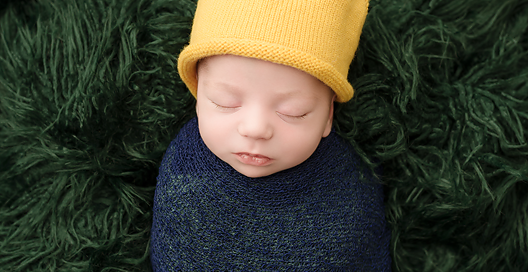 baby boy in blue wrap with yellow crown on green rug in kingston photography studio