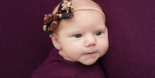 baby girl with eyes open in purple wrap on purple blanket with flower headband in kingston photography studio