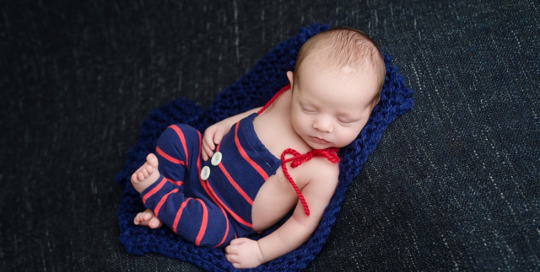 newborn baby boy in blue and red striped romper on navy blue blanket in ontario portrait studio_0005