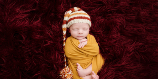 newborn boy in yellow wrap with striped hat on burgandy flokati rug in kingston photography studio_0003