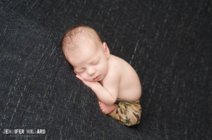 newborn boy with army camo pants on blue blanket in kingston ontario photography studio