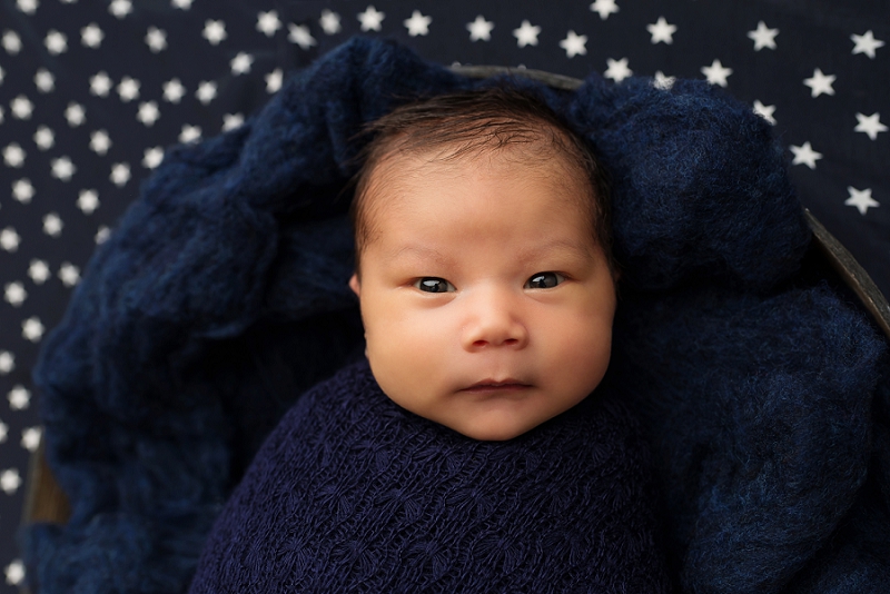 First Nations baby boy in navy blue wrap in black bowl up close on star backdrop by Belleville Newborn Photographer