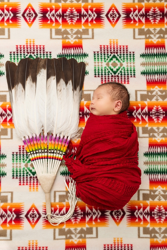 baby boy in red wrap on native multi-coloured blanket with native fan by Belleville Newborn Photographer