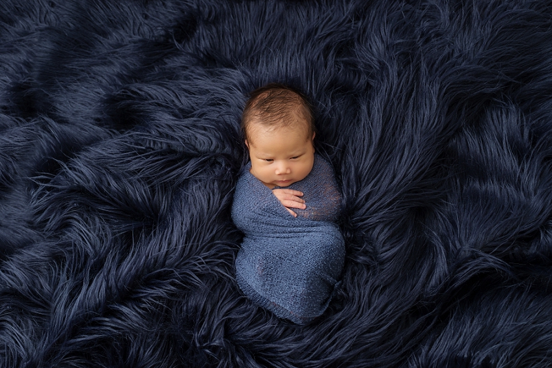 newborn baby boy in blue wrap on blue fur rug in black and white by Belleville Newborn Photographer