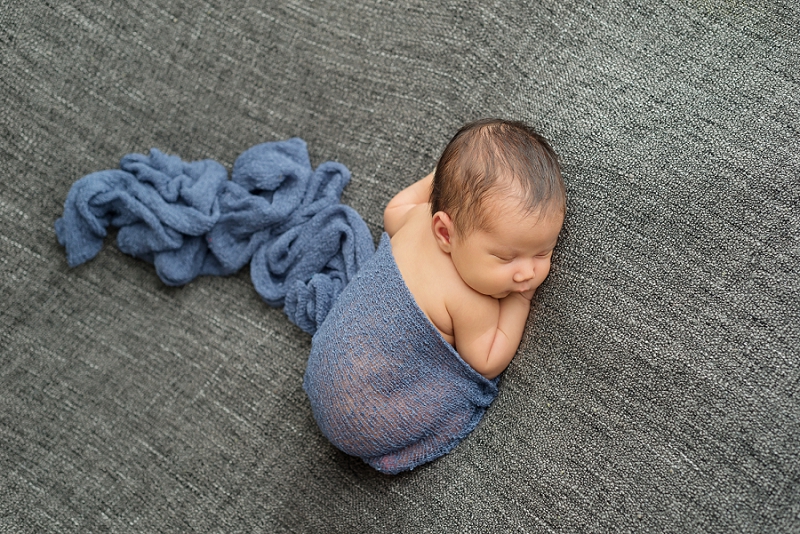 newborn baby boy in blue wrap on grey blanket from above by Belleville Newborn Photographer