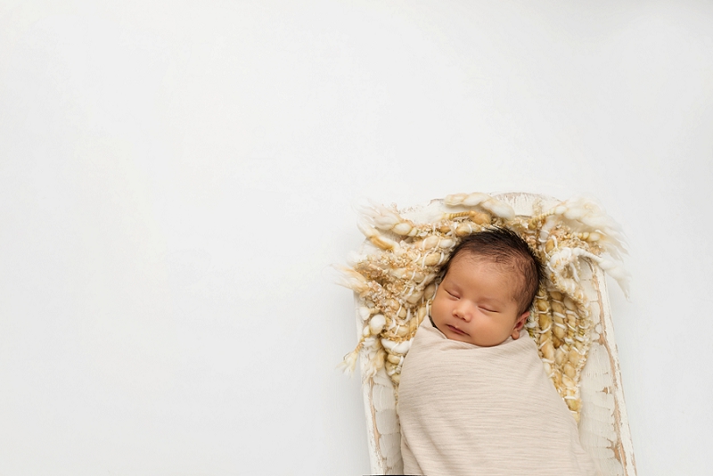 newborn baby in cream wrap on tan blanket on white wood trenchbowl on white backdrop with words by Belleville Newborn Photographer