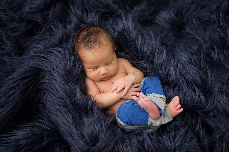 newborn boy in blue and grey striped pants on blue fur rug by Belleville Newborn Photographer