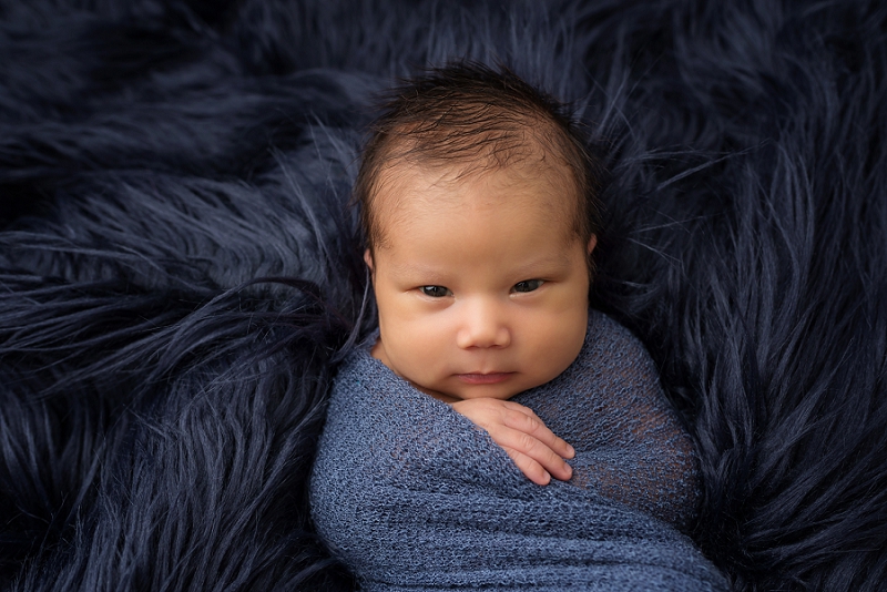 newborn boy in blue wrap on blue fur rug by Belleville Newborn Photographer