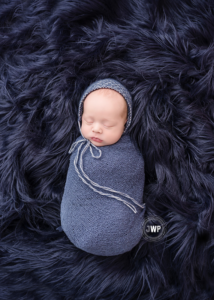 newborn-boy-in-blue-bonnet-and-blue-wrap-on-blue-flokati-rug-by-Kingston-Newborn-Photographer