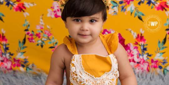 baby girl in mustard yellow romper with yellow and pink backdrop for first birthday Kingston baby photographer