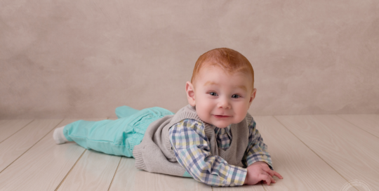 baby boy in blue pants with red hair on cream backdrop Kingston baby photographer