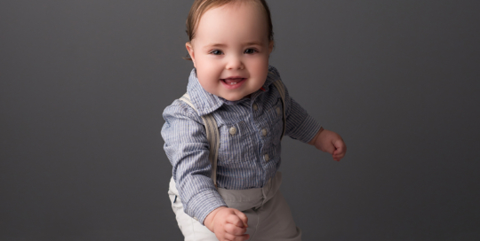 baby boy suspenders grey backdrop standing Kingston baby milestone photographer