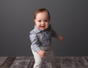 baby boy suspenders grey backdrop standing Kingston baby milestone photographer