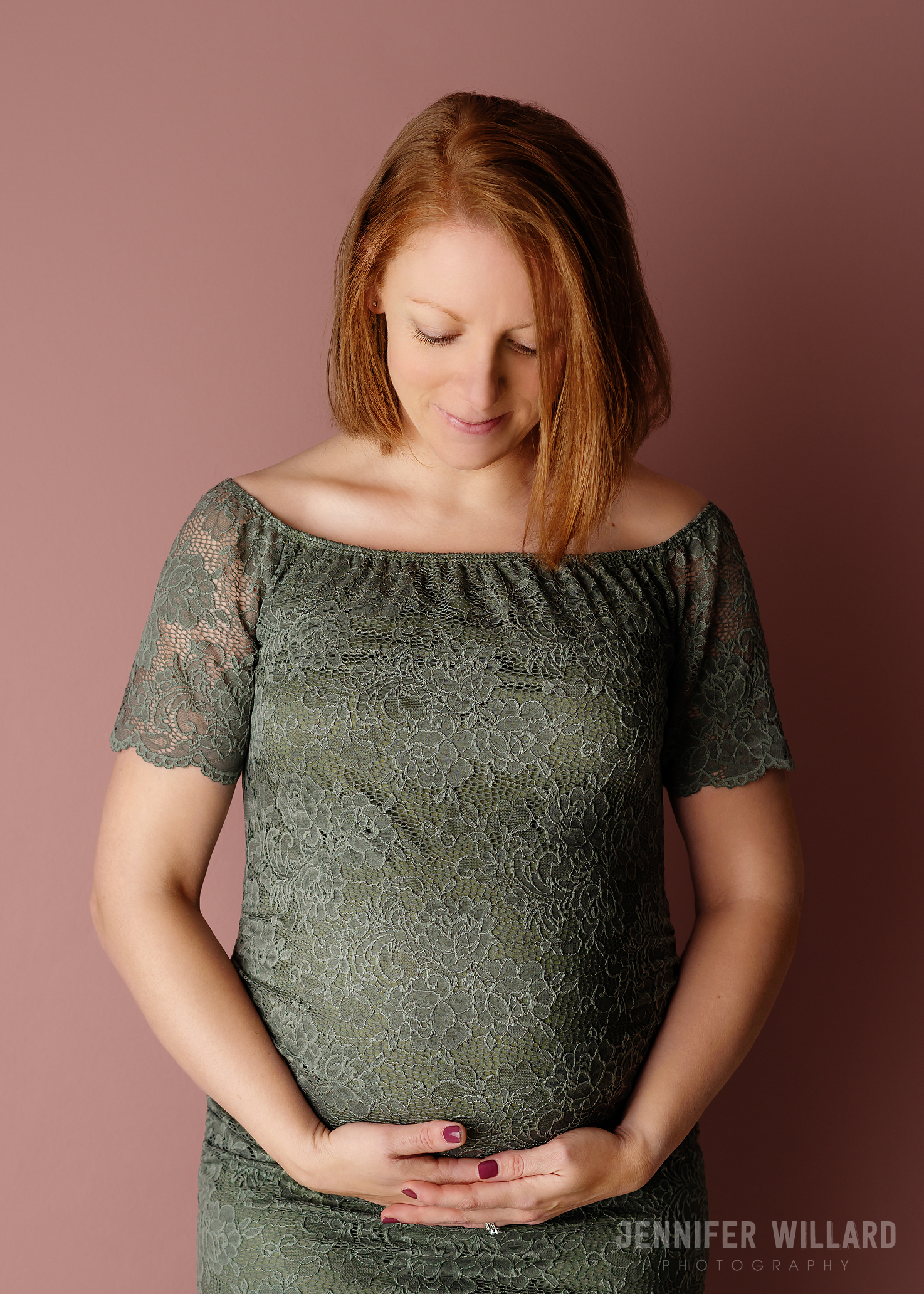 olive green lace dress on redhead Mom in studio with pink backdrop